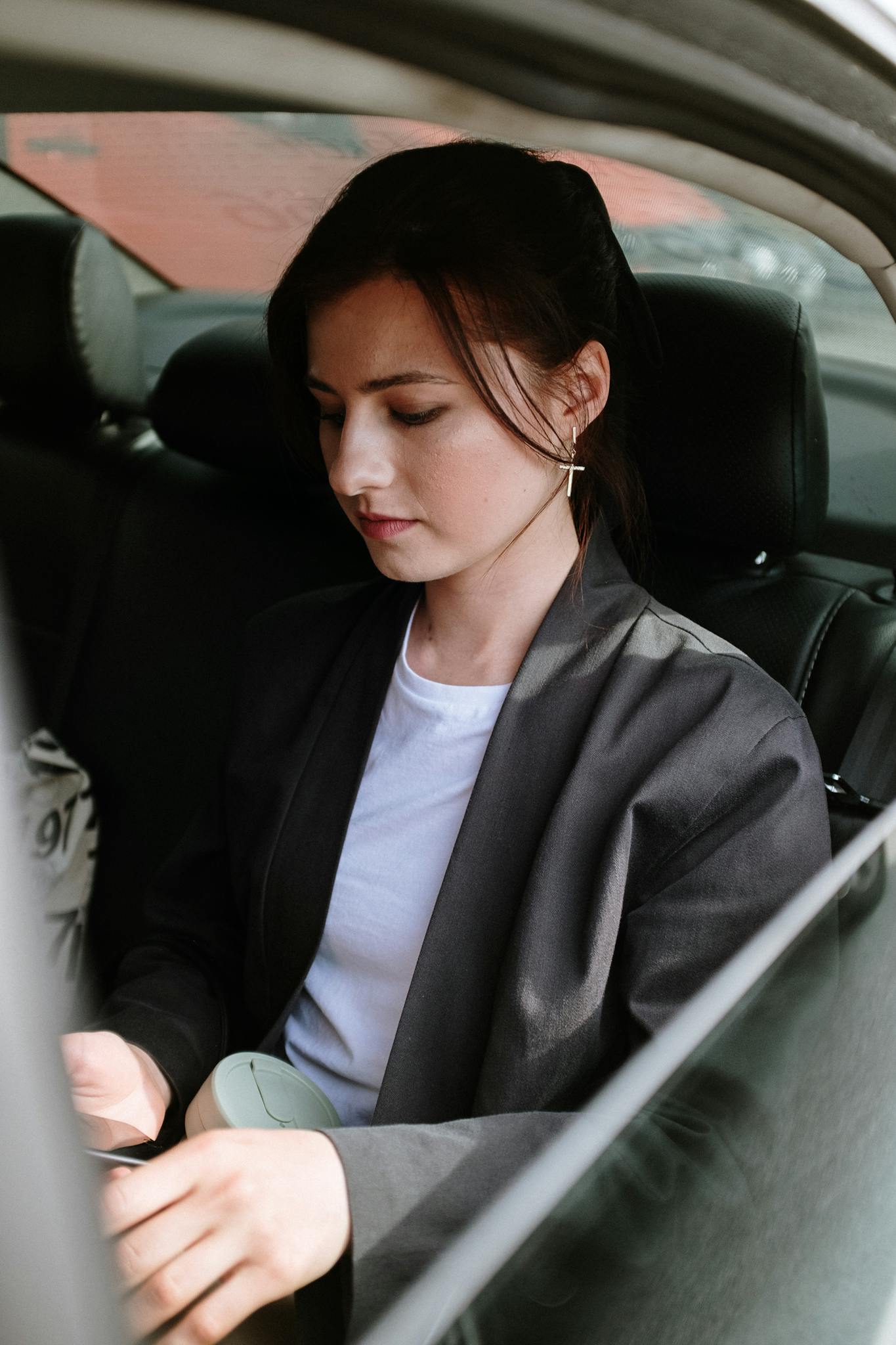 A woman in business attire using her smartphone while seated in a car, highlighting modern connectivity.